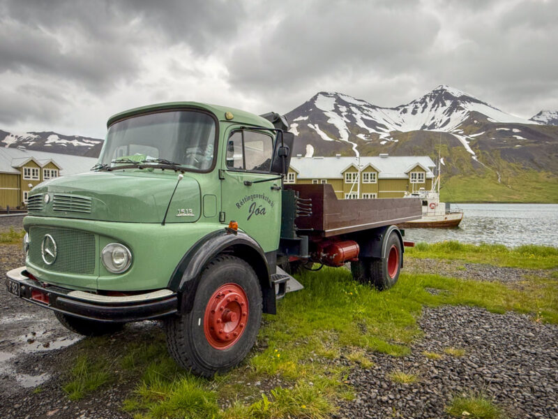 A flatbed truck in front of the Siglufjörður harbor with the snow-streaked mountains behind it.