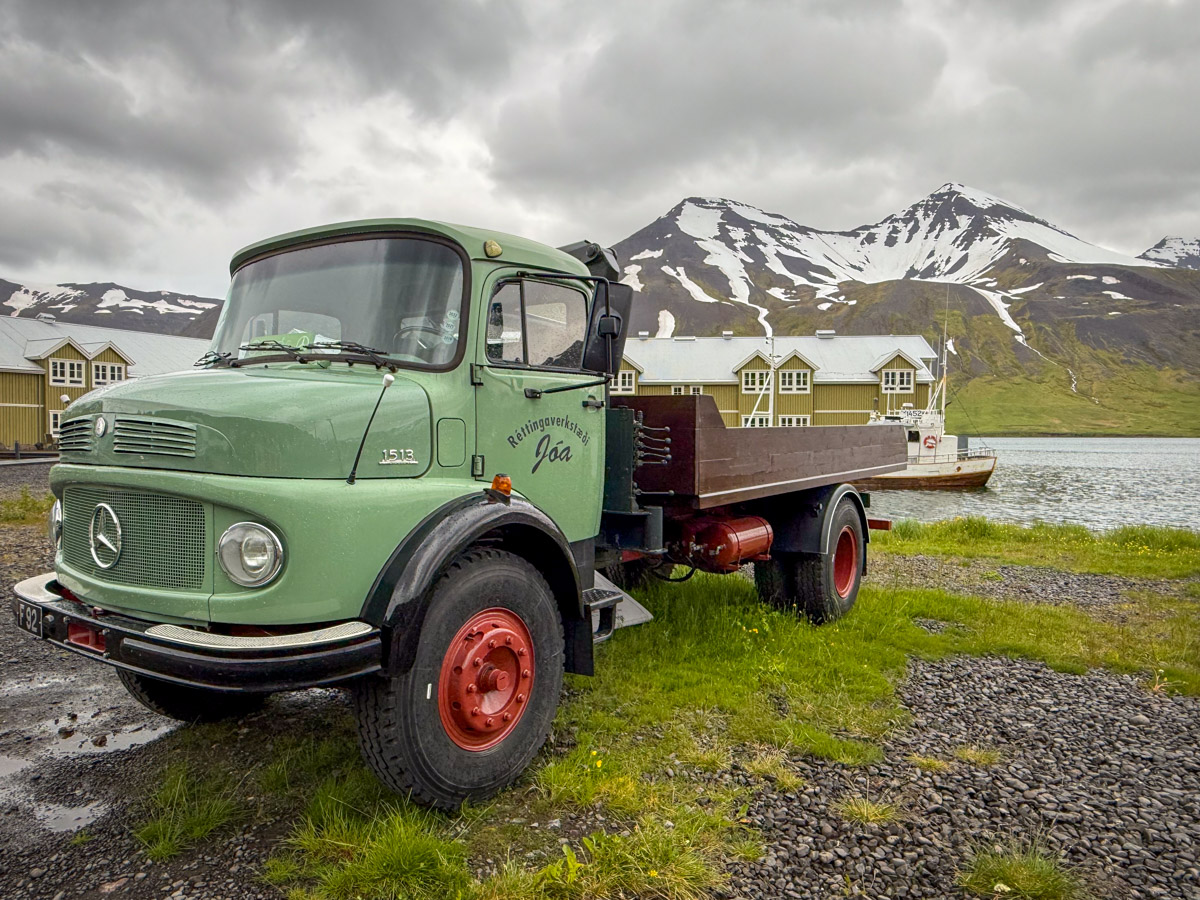A flatbed truck in front of the Siglufjörður harbor with the snow-streaked mountains behind it.